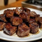 Tender, juicy steak bites cooked in a rich sauce, served in a bowl with a garnish of fresh herbs.