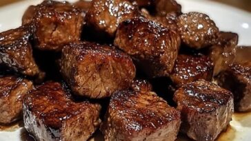 Tender, juicy steak bites cooked in a rich sauce, served in a bowl with a garnish of fresh herbs.