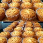 A batch of golden-brown cupcake cheese muffins with a fluffy texture and a cheesy topping, arranged on a wooden surface.