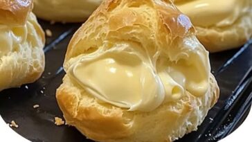 Light and airy cream puffs filled with fluffy whipped cream, dusted with powdered sugar on a plate.