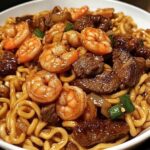 Garlic butter steak and shrimp stir-fried noodles garnished with green onions and sesame seeds.