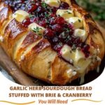 Garlic herb sourdough bread loaf sliced in a crosshatch pattern, stuffed with melted brie cheese and cranberry sauce, garnished with fresh herbs.