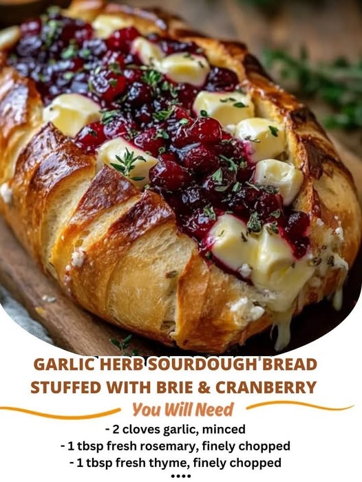 Garlic herb sourdough bread loaf sliced in a crosshatch pattern, stuffed with melted brie cheese and cranberry sauce, garnished with fresh herbs.