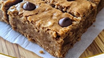 Stack of healthy peanut butter Greek yogurt blondies on a white plate, drizzled with peanut butter and sprinkled with oats.