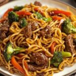 A bowl of homemade beef lo mein with tender slices of beef, stir-fried noodles, colorful bell peppers, carrots, and green onions, all coated in a glossy savory sauce.