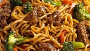 A bowl of homemade beef lo mein with tender slices of beef, stir-fried noodles, colorful bell peppers, carrots, and green onions, all coated in a glossy savory sauce.