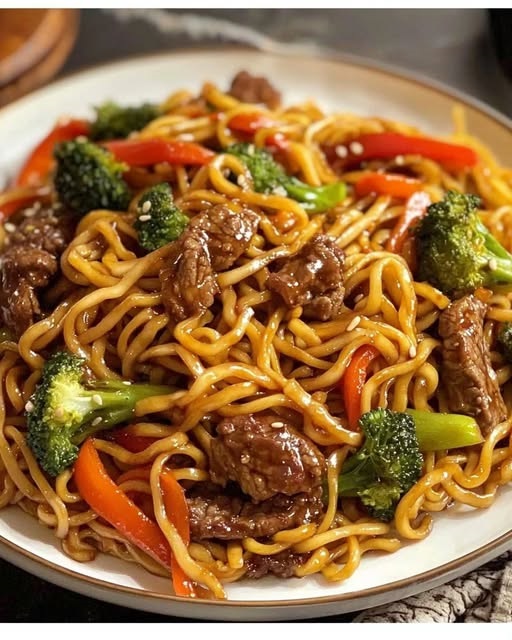 A bowl of homemade beef lo mein with tender slices of beef, stir-fried noodles, colorful bell peppers, carrots, and green onions, all coated in a glossy savory sauce.