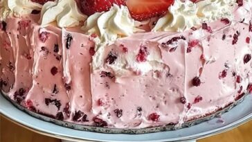 A slice of strawberry Italian cream pound cake topped with fresh strawberries and whipped cream on a white plate.