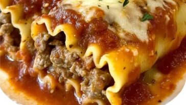 Italian meatball lasagna roll-ups on a white plate, covered in marinara sauce and melted cheese, garnished with fresh basil.