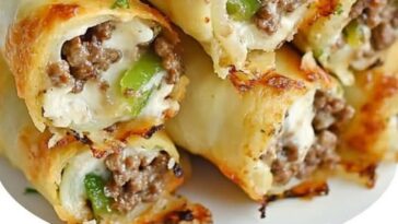 Keto Philly Cheesesteak roll-ups featuring thinly sliced steak, sautéed bell peppers, onions, and melted cheese, all wrapped in a low-carb, flourless wrap, garnished with fresh herbs.