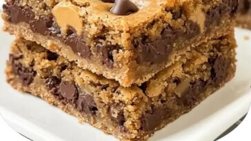 A close-up of chewy peanut butter chocolate chip cookie bars, with chocolate chips and a golden-brown crust, sliced into squares.