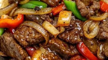 Pepper steak stir fry with colorful bell peppers and onions served over a bed of white rice.
