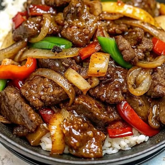 Pepper steak stir fry with colorful bell peppers and onions served over a bed of white rice.