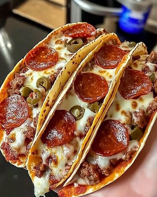 Close-up of pepperoni pizza tacos, with golden crispy taco shells filled with melted cheese, marinara sauce, and slices of pepperoni, garnished with fresh basil.
