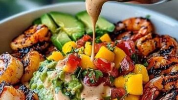 vibrant shrimp and avocado bowl topped with fresh mango salsa, creamy avocado slices, and a drizzle of lime-chili sauce, served in a bowl.