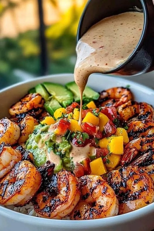 vibrant shrimp and avocado bowl topped with fresh mango salsa, creamy avocado slices, and a drizzle of lime-chili sauce, served in a bowl.