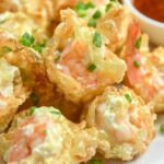 Crispy golden wontons filled with shrimp and cream cheese, arranged on a plate with a dipping sauce on the side.