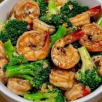 Stir-fried shrimp and broccoli with a savory sauce, served in a bowl with a garnish of sesame seeds and fresh green onions.