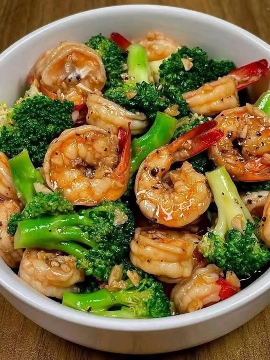 Stir-fried shrimp and broccoli with a savory sauce, served in a bowl with a garnish of sesame seeds and fresh green onions.