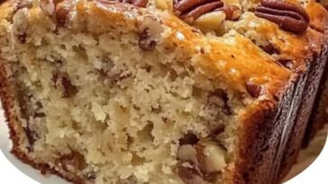 Golden-brown slices of Sweet Alabama Pecan Bread with visible chunks of pecans, sitting on a rustic wooden table