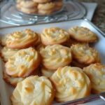 Golden, buttery cookies arranged neatly on a baking tray, some dusted lightly with powdered sugar.