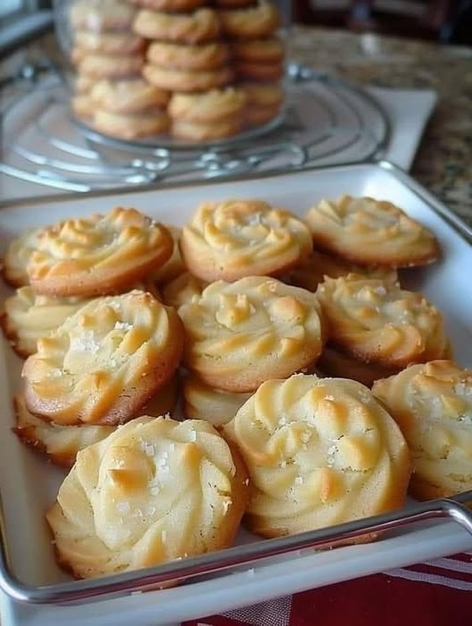 Golden, buttery cookies arranged neatly on a baking tray, some dusted lightly with powdered sugar.