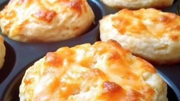 A plate of golden, fluffy mini cheesy biscuits with a lightly crisp top and specks of melted cheddar cheese throughout.