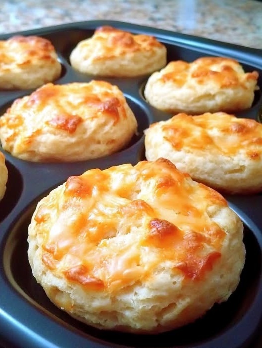 A plate of golden, fluffy mini cheesy biscuits with a lightly crisp top and specks of melted cheddar cheese throughout.