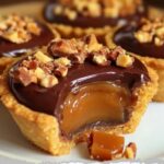 Mini caramel pies topped with crumbled Butterfinger candy on a graham cracker crust, arranged on a white serving tray.