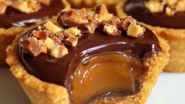 Mini caramel pies topped with crumbled Butterfinger candy on a graham cracker crust, arranged on a white serving tray.