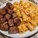 Cajun-seasoned steak tips served over cheesy rigatoni in a creamy Parmesan sauce, garnished with herbs.