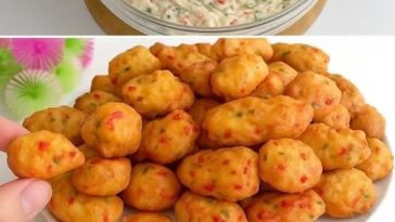 Golden-brown cheesy vegetable fritters stacked on a plate, garnished with fresh herbs and served with a side of dipping sauce.