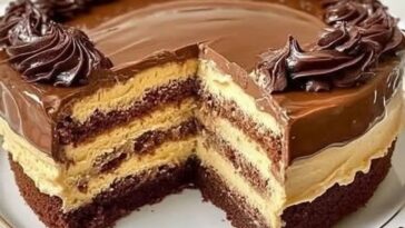A rich chocolate cake layered with cream cheese filling, topped with a glossy chocolate glaze and garnished with chocolate shavings and a dusting of powdered sugar.