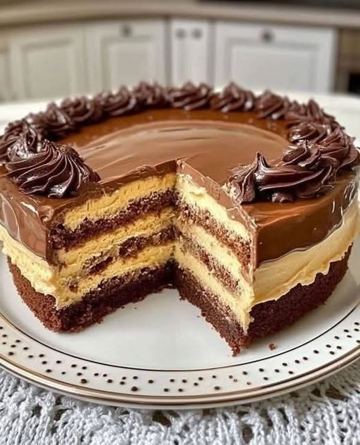 A rich chocolate cake layered with cream cheese filling, topped with a glossy chocolate glaze and garnished with chocolate shavings and a dusting of powdered sugar.