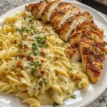 Creamy garlic Parmesan chicken served over cheesy twisted pasta on a white plate, garnished with fresh parsley.