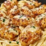 Creamy Parmesan pasta topped with sautéed garlic butter chicken, garnished with fresh herbs.