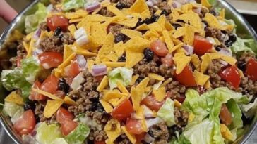 A vibrant bowl of Dorito taco salad with layers of taco meat, lettuce, tomatoes, cheese, and crunchy Doritos.