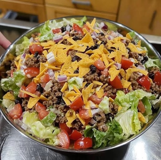 A vibrant bowl of Dorito taco salad with layers of taco meat, lettuce, tomatoes, cheese, and crunchy Doritos.