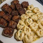 Garlic butter steak bites served with cheese-filled tortellini in a creamy Alfredo sauce, garnished with herbs.