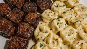 Garlic butter steak bites served with cheese-filled tortellini in a creamy Alfredo sauce, garnished with herbs.