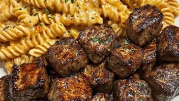 A plate of garlic butter steak bites served alongside twisted pasta coated in creamy spicy Cajun Alfredo sauce, garnished with parsley.