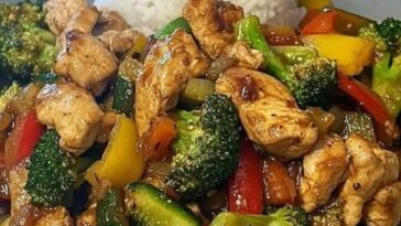 A colorful garlic chicken and vegetable stir-fry served over a bed of creamy rice on a white plate.