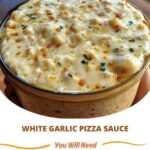 A small bowl of thick, creamy garlic pizza sauce garnished with herbs, surrounded by pizza ingredients like dough and cheese.