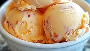 A bowl of creamy homemade peach ice cream garnished with fresh peach slices and a sprig of mint.