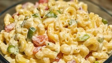 A bowl of creamy macaroni salad mixed with chopped jalapeños, crispy bacon, and a sprinkle of shredded cheddar cheese, topped with a dollop of sour cream.