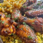 A plate featuring crispy lemon pepper chicken wings, fluffy yellow rice, and creamy macaroni and cheese, served as a hearty, comforting meal.