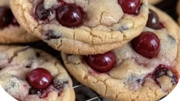 Soft cookies studded with chocolate chips and chopped maraschino cherries, stacked on a plate with a glossy red cherry on top.