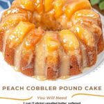 "A thick slice of peach cobbler pound cake topped with a peach glaze and caramelized peach slices, sitting on a white plate with a fork beside it."