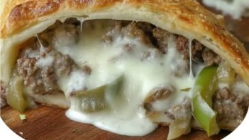 Golden-brown Philly cheesesteak stromboli roll-up, sliced to reveal the cheesy beef filling, on a cutting board.
