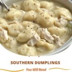 A pot of Southern-style dumplings simmering in rich chicken broth, with soft dough pieces floating among shredded chicken.